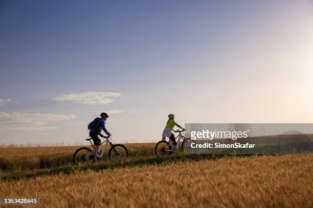 couple riding bicycle uphill on rural field - uphill stockfoto's en -beelden