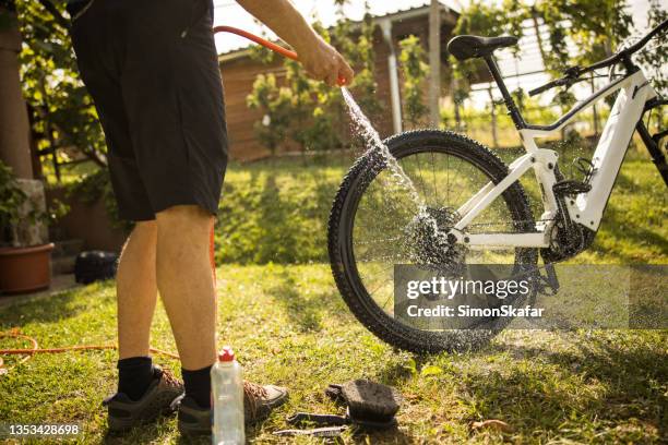 niedriger teil des mannes, der das fahrrad mit rohrwasser wäscht - dirty bike stock-fotos und bilder