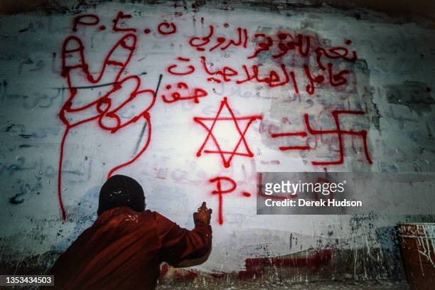 View, from behind, of an unidentified Pro-Palestinian activist spray painting pro-PLO and anti-Israeli graffiti on a wall during the First Intifada,...