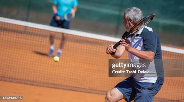 two senior men spending active day playing tennis on tennis court - senior tennis stock pictures, royalty-free photos & images