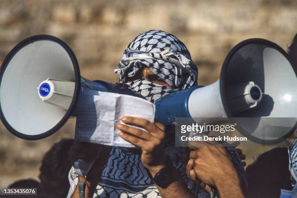 Close-up of an unidentified Pro-Palestinian activist, his head mostly covered by a black and white keffiyeh, as he recites a speech through a pair of...