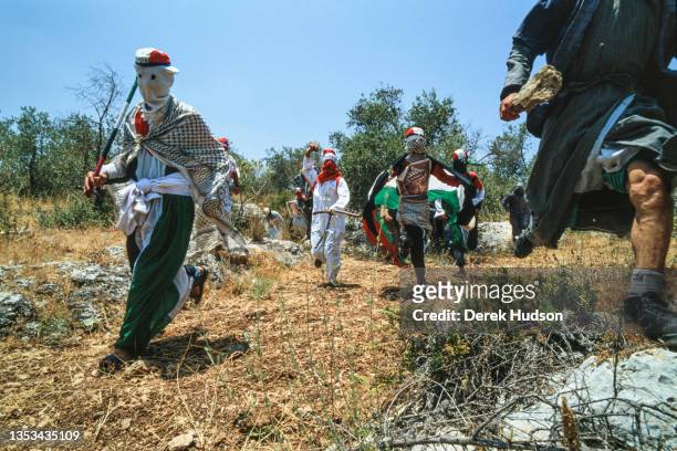 View of a group of hooded and masked Pro-Palestinian activists, some dressed in the colors of the Palestinian flag, as they run through an olive...
