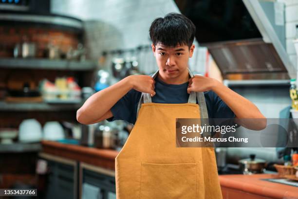 asian chinese teenager boy baker wearing apron at kitchen - kitchen straighten stockfoto's en -beelden
