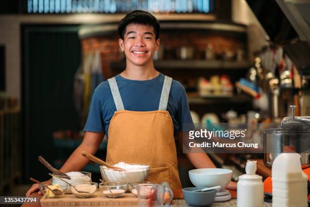 asian chinese smiling teenager boy baker looking at camera in the kitchen - chinese teenage boy stockfoto's en -beelden