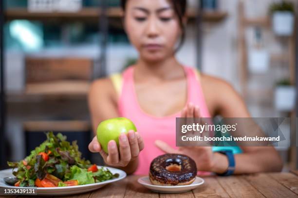 women push the donut plate that is a mixture of trans fat. and choose to hold the apple. don't eat junk food. diet concept - fat loss training stockfoto's en -beelden