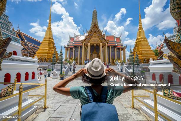 woman traveler with white backpack and hat on sunny day. look at the temple “wat phra kaew”and background from bangkok thailand. traveling concepts in thailand. - art culture and entertainment stockfoto's en -beelden