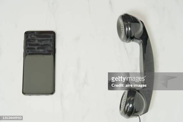 closeup shot of a black phone handset and a black smartphone on a white table background - obsolete software stock pictures, royalty-free photos & images