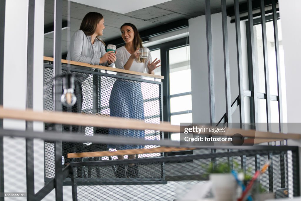 Two female business colleagues chatting over coffee at the modern office