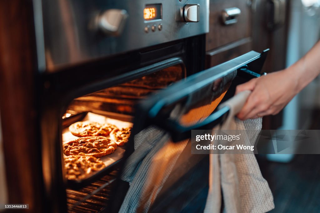 Cropped shot of female hand opening the oven door while baking cookies in the oven