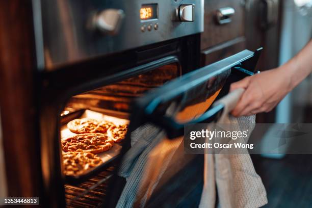 cropped shot of female hand opening the oven door while baking cookies in the oven - pasticceria foto e immagini stock