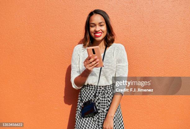 woman using mobile phone in front of orange wall - paris millenials stock-fotos und bilder