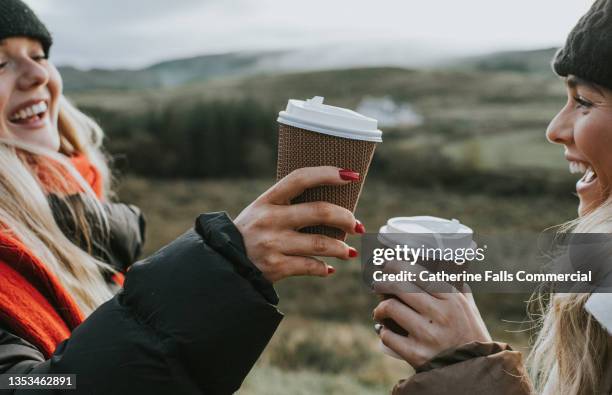 two beautiful young woman hold cardboard coffee cups and make a celebratory toast by bumping them together - takeaway coffee stockfoto's en -beelden