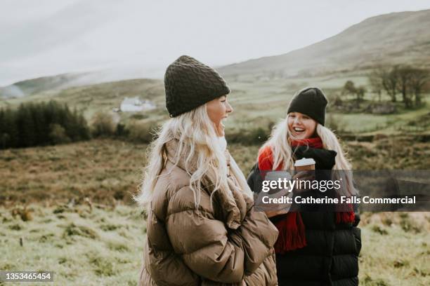 a woman is pleasantly surprised during an outdoor conversation with another woman, opening her mouth wide when she receives the exciting news - winterjacke stock-fotos und bilder