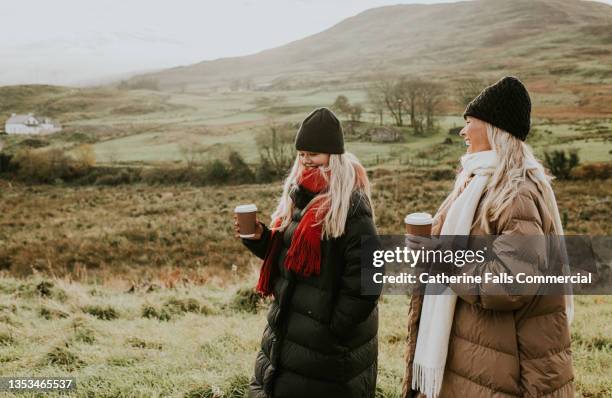 two, young, beautiful woman enjoy a walk outdoors, dressed in warm clothing, clutching takeaway coffee cups - puffer jacket photos et images de collection