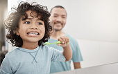Shot of an adorable little boy brushing his teeth in a bathroom with his father at home