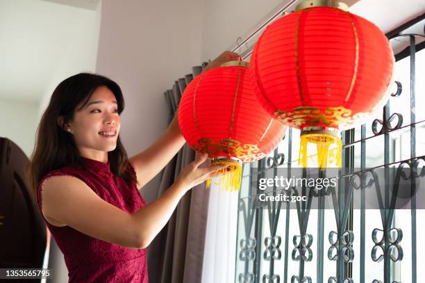 asian woman hanging big red lanterns at home and prepares to celebrate the chinese new year. - chinees lantaarnfeest stockfoto's en -beelden