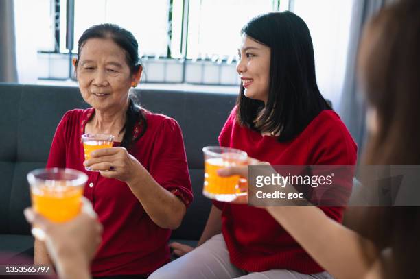 drei generationen glücklicher asiatischer familien genießen familientreffen und wiedersehen, während sie auf orangensaft anstoßen, um das chinesische neujahr zu feiern. - 30 year old female stock-fotos und bilder