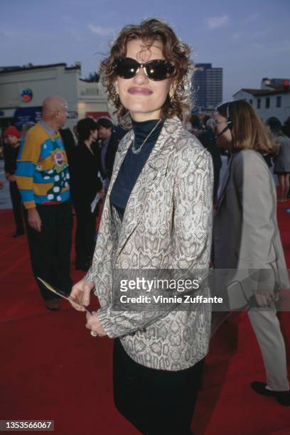 American actress and comedian Sandra Bernhard, wearing a grey leopard print-effect jacket over a dark blue turtleneck sweater and sunglasses, attends...