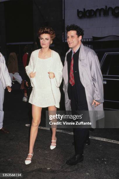 American actress and comedian Sandra Bernhard, wearing a white minidress, and American fashion designer Isaac Mizrahi, wearing a grey raincoat over a...