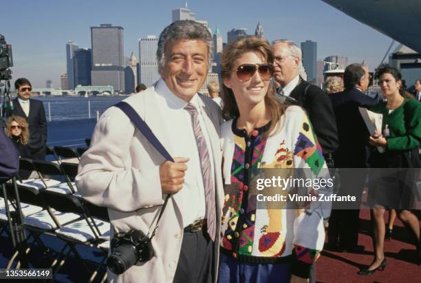 American singer Tony Bennett, wearing a white jacket over a shirt and tie, a camera on a strap over his right shoulder, and American schoolteacher...