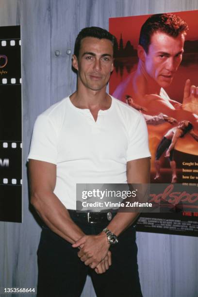 Swiss actor and model Daniel Bernhardt, wearing a short-sleeved collarless shirt, poses by a poster for his film 'Bloodsport II: The Next Kumite' at...