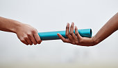 Shot of two athletes passing a baton during a relay race