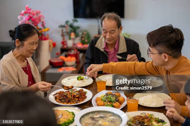 an asian man sharing food to his mother while enjoying reunion dinner at home during  chinese new year - 39 year old stockfoto's en -beelden