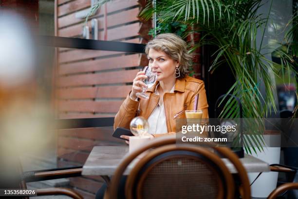 woman sitting in outdoor cafe and treating herself with latte after work - generation x stock pictures, royalty-free photos & images