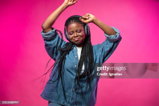 a young happy african blogger with afro braids and headset on her head dances and sings with closed eyes on a pink background - presentator amusement stockfoto's en -beelden