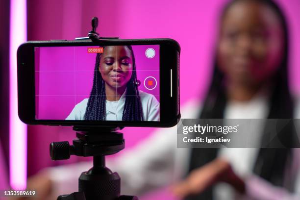 a backstage from the filming of a video blog in a home studio with a pink background and a smart phone screen with a dark-skinned blogger on it in the foreground of a picture - filmen stockfoto's en -beelden