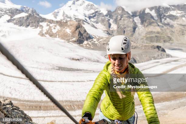 young woman on via ferrata climbing up, glacier behind - altitude training stock pictures, royalty-free photos & images