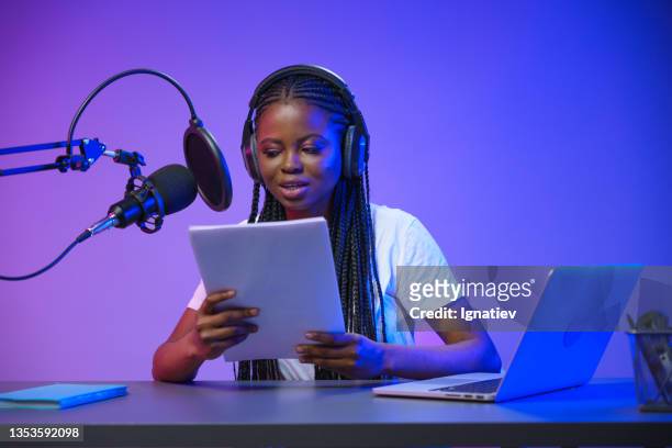 a young african female radio dj records the news in a professional studio with a purple background - radio dj stockfoto's en -beelden