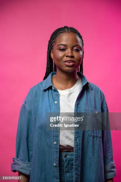 an attractive dark - skinned woman in a jeans shirt on a pink background - photo shoot set up stock pictures, royalty-free photos & images