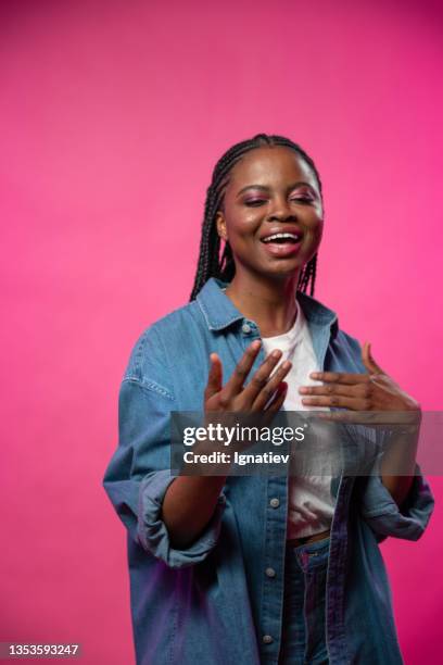 an attractive dark - skinned young singer in a jeans shirt and white t-shirt sings on camera, standing on a pink background, - photo shoot set up stock pictures, royalty-free photos & images