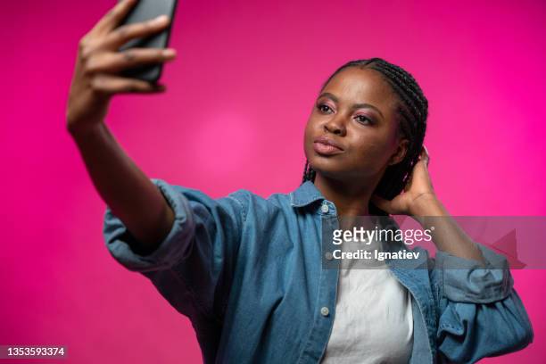 ayoung blogger with afro braids makes selfie on her smart phone on a pink background - atriz imagens e fotografias de stock