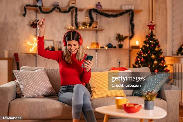 woman listening music on couch at christmas time - christmas music listen stock pictures, royalty-free photos & images