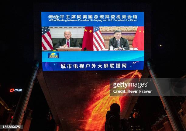 Large screen displays United States President Joe Biden, left, and China's President Xi Jinping during a virtual summit as people walk by during the...