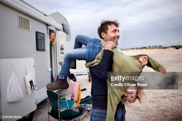 playful father carrying girl at camper van on the beach - life stock-fotos und bilder