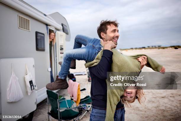 playful father carrying girl at camper van on the beach - family holiday fotografías e imágenes de stock