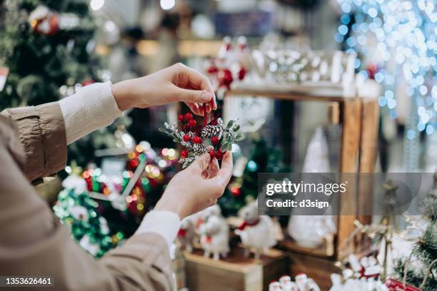 close up of young woman doing christmas shopping, holding a christmas wreath decoration in retail store in festive christmas season. countdown to christmas, festival and celebration concept - marché de noël photos et images de collection