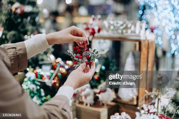close up of young woman doing christmas shopping, holding a christmas wreath decoration in retail store in festive christmas season. countdown to christmas, festival and celebration concept - julmarknad bildbanksfoton och bilder