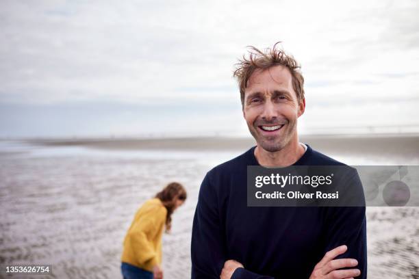 portrait of happy man on the beach with daughter in background - kust karakteristiek stockfoto's en -beelden