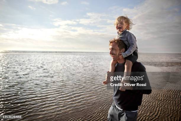 happy father carrying son on shoulders on the beach - north sea wind stock pictures, royalty-free photos & images