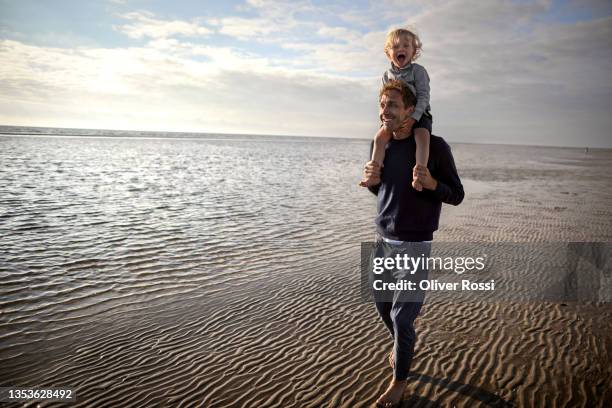happy father carrying son on shoulders on the beach - 肩に乗せる ストックフォトと画像