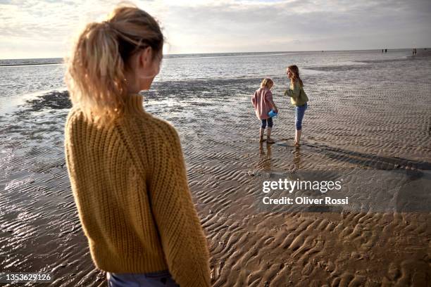 mother looking at two daughters on the beach - ebbe stock-fotos und bilder
