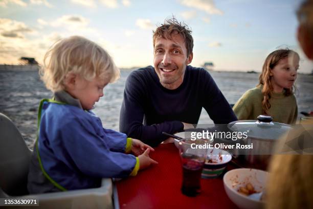 portrait of smiling father sitting at camping table with fanily - familie camping stock-fotos und bilder