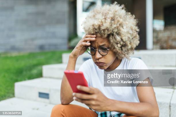 afro woman looking worried and stress while reading bad news on her mobile phone. - emotional stress stock-fotos und bilder