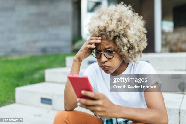 afro woman looking worried and stress while reading bad news on her mobile phone. - female worried mobile imagens e fotografias de stock