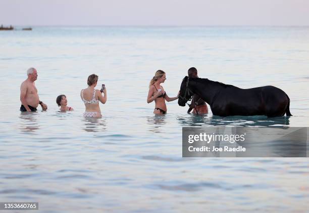 Tourists look on as horse trainers wade in the sea with horses from the Garrison Savannah horse racing track home to the Barbados Turf Club on...