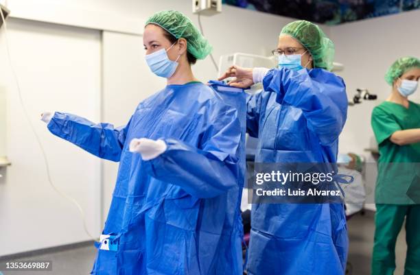 medical assistant helping a surgeon put on sterile clothes in an operating room - operating gown fotografías e imágenes de stock